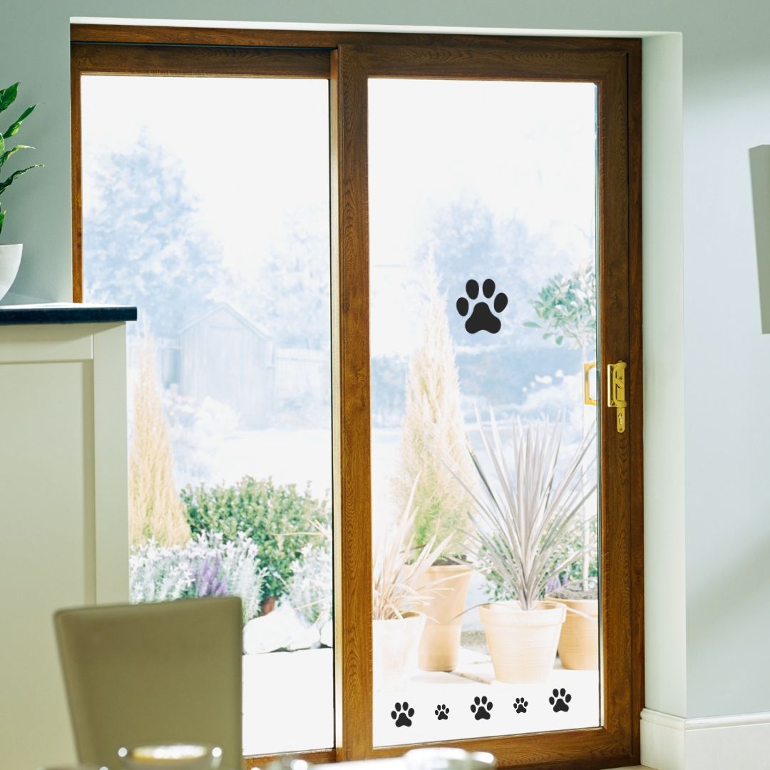 A set of stylish black paw print vinyl stickers applied to a glass sliding door, showcasing their high-quality design and versatility for decorating various surfaces.